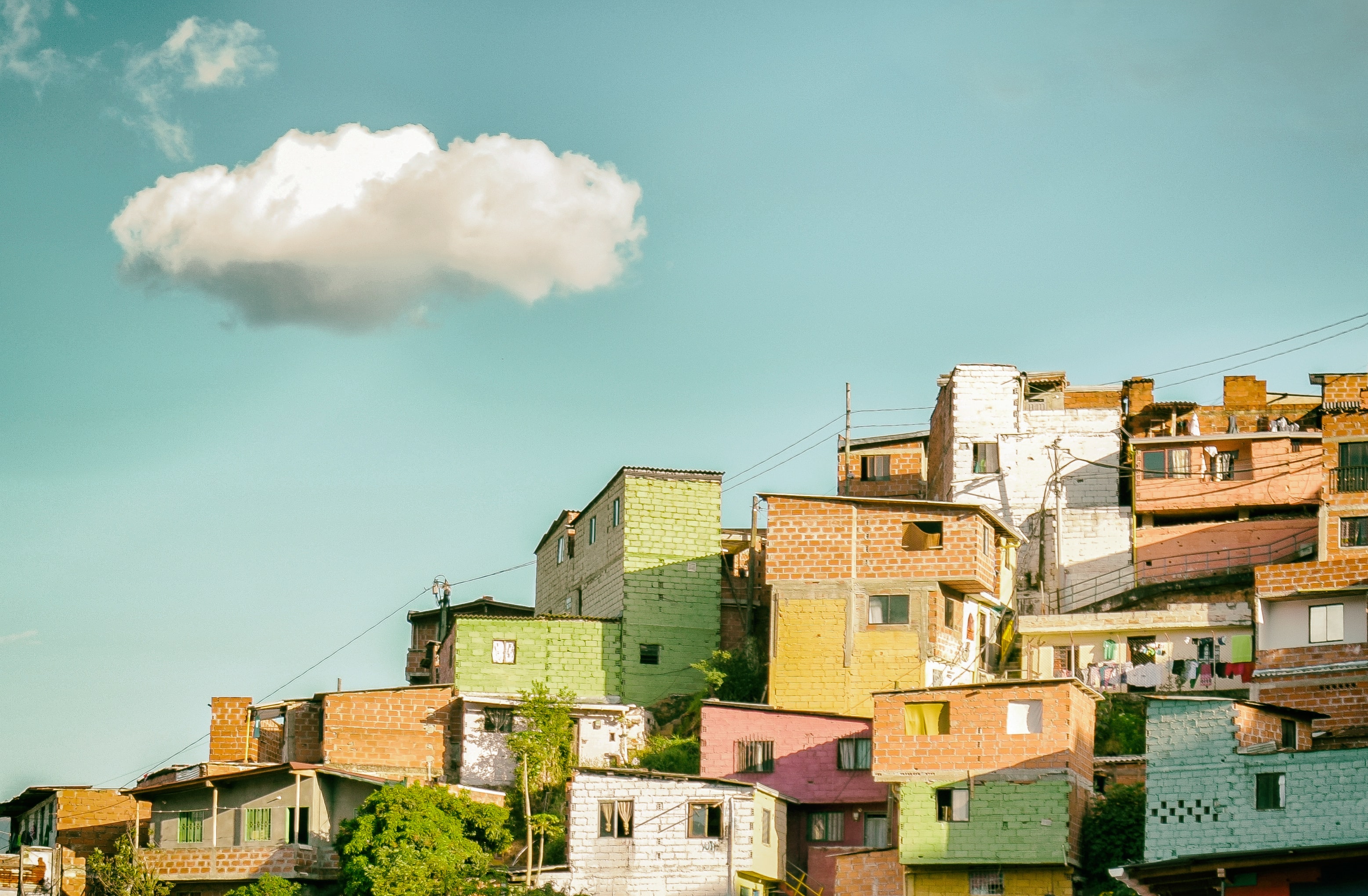 Brick houses painted in various colours on a hillside, against a blue sky with a single white-grey cloud.